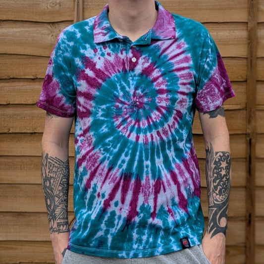 Person wearing a tie-dye shirt with a spiral pattern standing against a wooden fence.