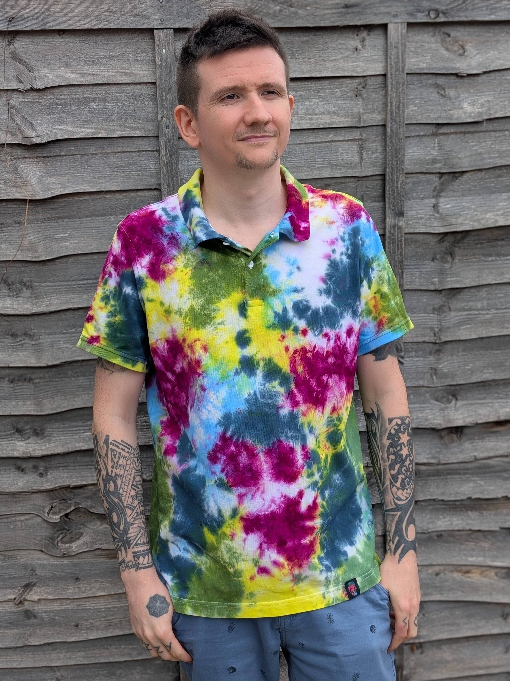 Man wearing a tie-dye shirt standing against a wooden fence