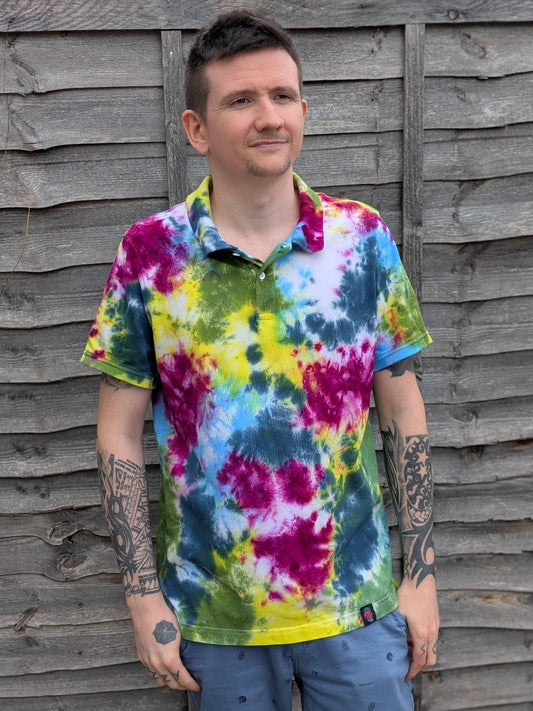 Man wearing a tie-dye shirt standing against a wooden fence