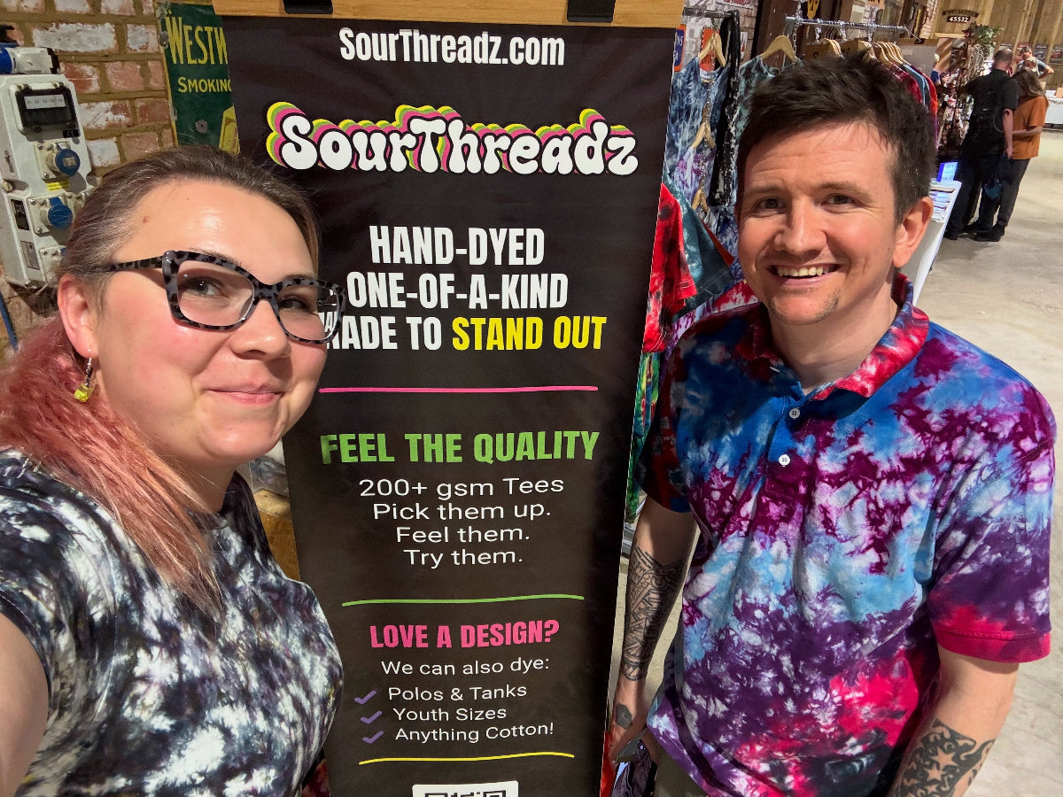 Two people standing next to a 'Sour Threadz' banner with tie-dye products.